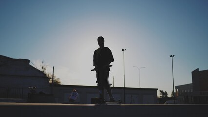 guy riding a skateboard. city landscape glare of the sun. height extreme. brave guy jumping high on...