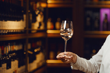 Close up female hand hold poured glass with white wine on cellar background with a free copy space.