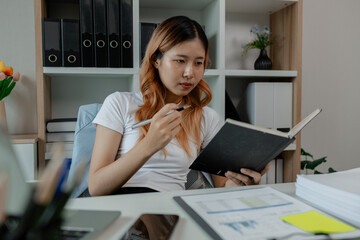 a businesswoman is working in her office and writing a note, a female employee is writing a brief summary of a report so that she will not forget, working in workplace while work hours