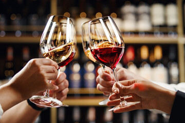 Big company people clinking glasses with red, rose and white wine on blurred cellar background. Men and women cheers with alcohol drink, closeup