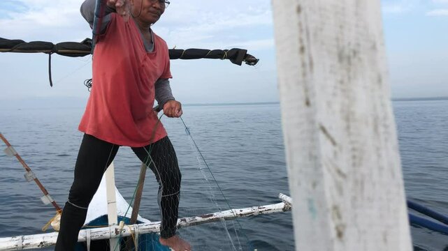 Fisherman on a wooden boat is pulling in a fishing net from the depths of the sea