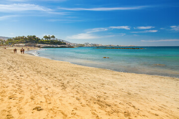 A picturesque beach scene from Playa Del Duque, Tenerife, showcasing turquoise waters gently caressing the sandy shore