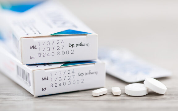 Close-up of the production code and expiration date printed on the side of a medicine box, with pills placed on a table. The image highlights the importance of checking medication before consumption