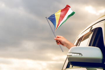 Waving the Seychelles flag against the sunrise or sunset from a car driving along a country road. Holding the Seychelles flag, traveling by car, on a weekend trip.
