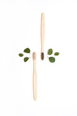 Bamboo wooden eco toothbrushes and green leaves on white background top view. Eco-friendly hygiene products without plastic. Treatment of teeth and gums, natural accessories for oral cavity