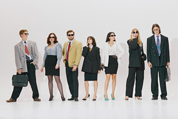 Obraz premium Posing confidently, business team showcases oversized suits and trendy accessories against white studio background. Concept of corporate culture, business and style, leadership. Ad