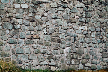 Natural stone wall partially covered with green plants