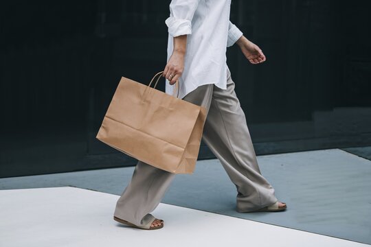 Stylish Shopper: A woman strolls confidently, carrying a large kraft paper shopping bag, showcasing effortless style and modern consumerism.