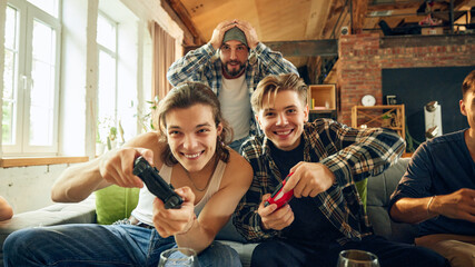 Close-up of two players intensely focused on competition on TV screen. Game getting serious, and victory just button away. Concept of football fans, sport evens, cybersport.