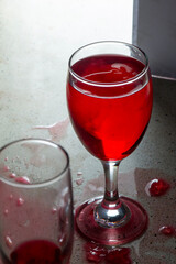 A glass of red liquid was placed next to a glass of wine that was empty and spilled on the granite...