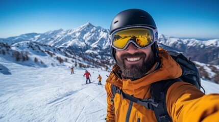 A smiling skier takes a selfie at the top of a ski slope in a winter mountain landscape with snow-covered peaks and a blue sky