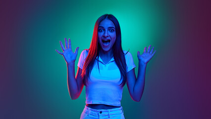 Shocked young girl, dressed stylish, casual clothes raises hands and shouting in neon light against gradient studio background. Concept of human emotions, business, beauty and fashion, sales season.