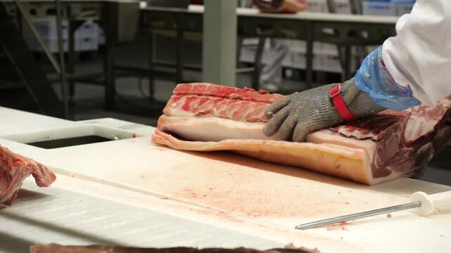 Butcher cuts skin off the slab of pork at meat processing factory