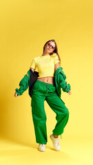 In bright yellow top and green pants, she strikes pose, layering with green jacket. Her cool style radiates against vibrant backdrop. Concept of beauty and fashion, sales season.