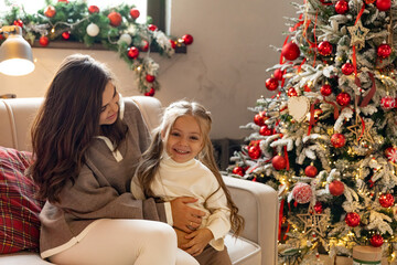 Cheerful excited mom and kid girl playing on sofa, tickling each other, laughing, having fun near...