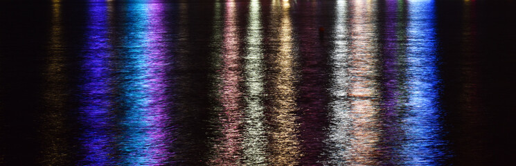Color photography of bright color lights reflection on water by night