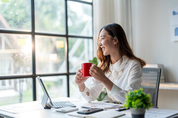 Businesswoman smiling and drinking coffee while looking out of office window