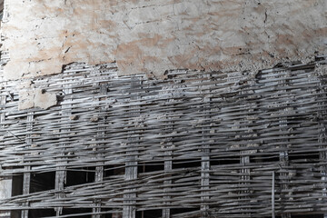 A weathered brick wall with peeling plaster and exposed red bricks. A row of woven bamboo sticks forms the top of the wall.