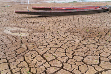 The ground is cracked and parched, with a network of deep fissures. Several traditional wooden boats are beached on the dried-up water body, highlighting the severity of the drought.