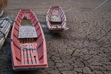 The ground is cracked and parched, with a network of deep fissures. Several traditional wooden boats are beached on the dried-up water body, highlighting the severity of the drought.
