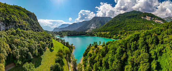 A picturesque view of a lake Lago di Tenno surrounded by mountains, with a tree-covered island in the center. An ideal spot for relaxation, connecting with nature, and recreation.