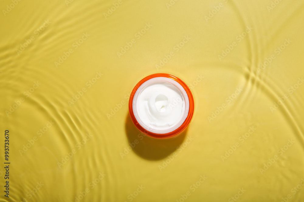 Poster Jar with cream in water on yellow background, top view. Cosmetic product