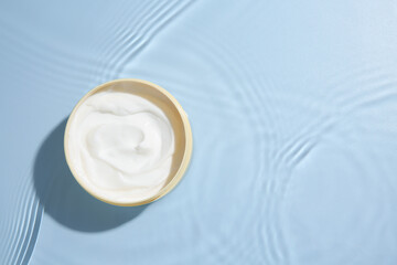 Cosmetic product. Jar with cream in water on light blue background, top view. Space for text