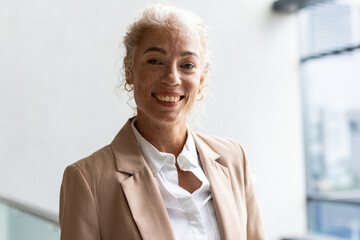 Smiling businesswoman in blazer standing confidently in modern office environment