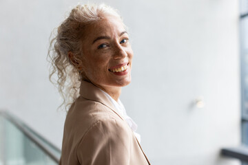 Fototapeta premium Smiling woman in business attire looking confidently at camera in office setting, copy space