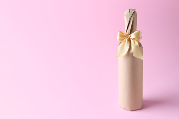 Wine bottle in burlap bag with satin bow on pink background. Space for text