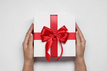 Woman holding gift box with bow on white background, top view