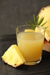 Tasty pineapple juice in glass and slice of fresh fruit on wooden table, closeup