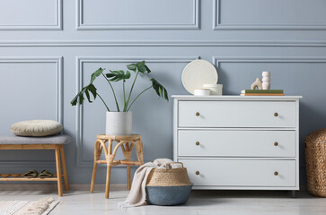 Stylish interior with stool and chest of drawers near light grey wall