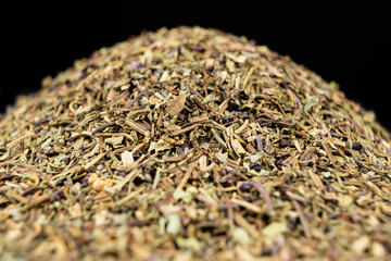 Pile of chopped dry basil seasoning on a black background.