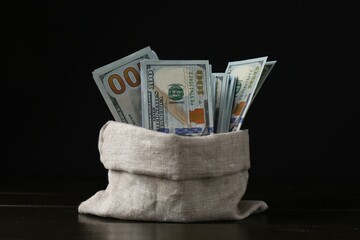 Dollar banknotes in sack on wooden table against black background