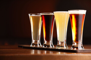 Glasses with different types of beer on wooden table against color background, closeup
