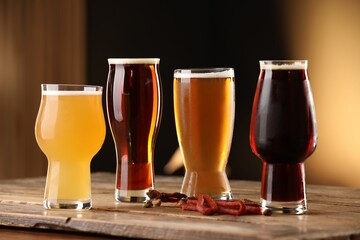 Glasses with different types of beer and snacks on wooden table against color background