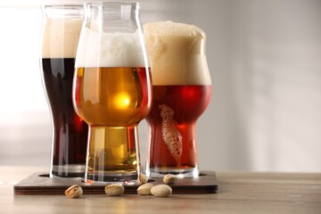 Glasses with different types of beer and pistachio nuts on wooden table indoors, closeup. Space for text