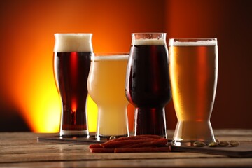 Glasses with different types of beer and snacks on wooden table against color background