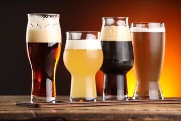 Glasses with different types of beer on wooden table against color background, closeup