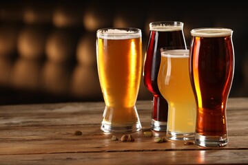 Glasses with different types of beer and pistachio nuts on wooden table indoors, space for text