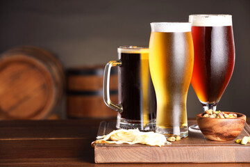 Glasses with different types of beer and snacks on wooden table in bar. Space for text