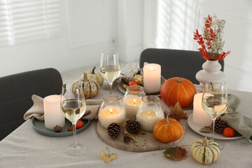 Autumn place setting with burning candles, glasses of wine and decor on table indoors