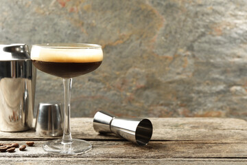 Delicious espresso martini with coffee beans in glass and bartender equipment on wooden table,...