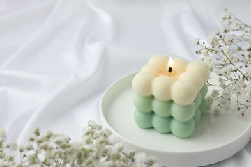 Stylish bubble candle and gypsophila flowers on white cloth, closeup. Space for text