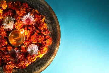Diwali celebration. Diya lamp and beautiful flowers on turquoise background, top view. Space for...