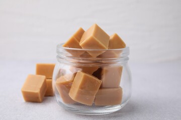 Tasty sweet caramel candies in glass jar on light table, closeup