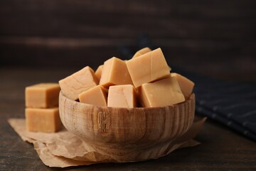 Tasty sweet caramel candies in bowl on wooden table