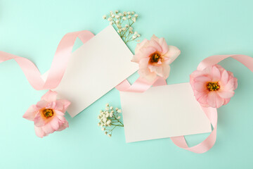 Floral composition with blank cards, flowers and ribbon on turquoise background, flat lay