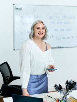 Portrait of a young beautiful English teacher working at school, at her desk in the classroom.